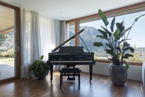 Black baby grand piano in a living room with a big window looking out on a lake