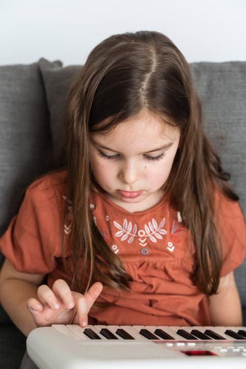 Young girl sitting on couch with miniature keyboard on lap learning to play piano