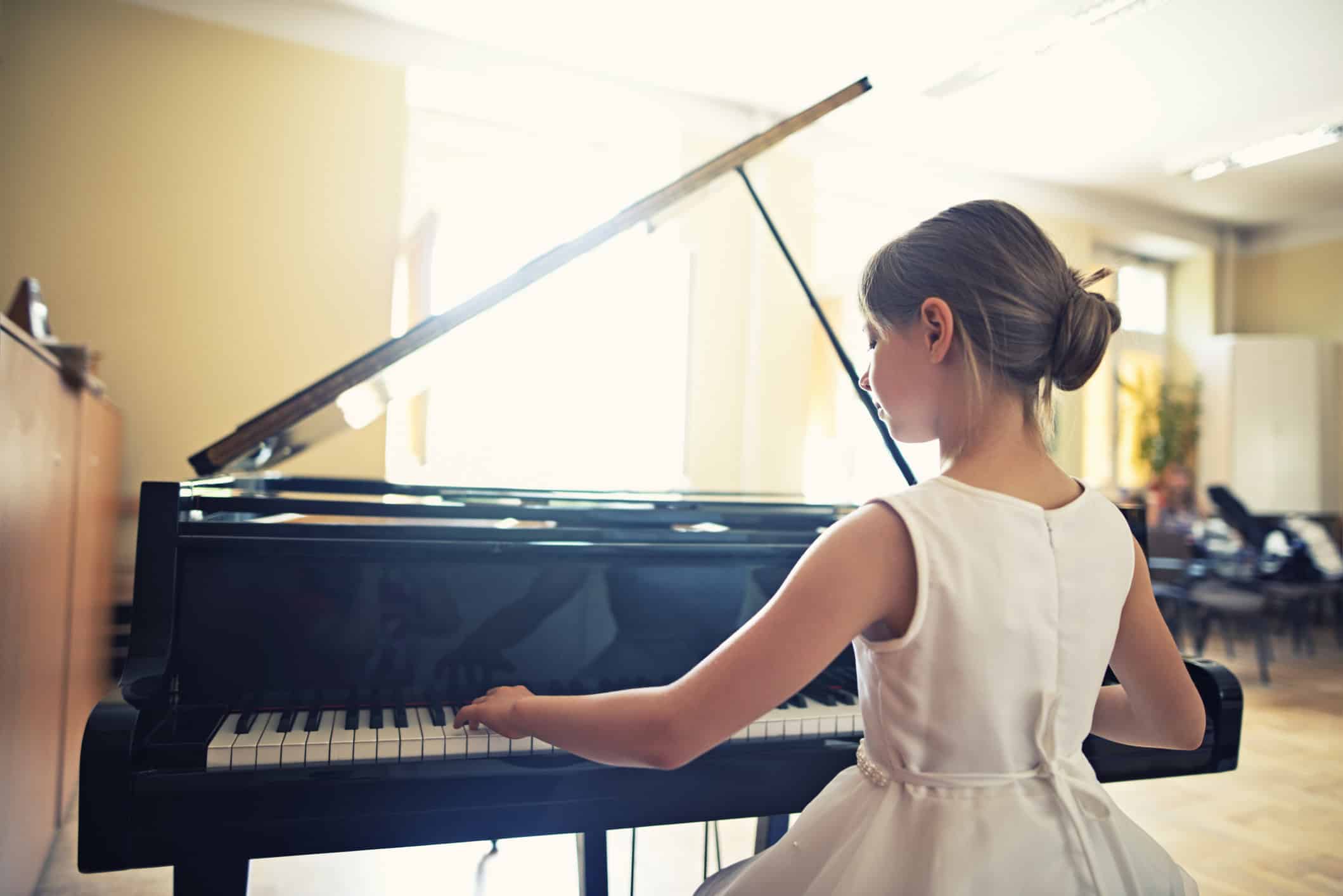 Young girl in white dress playing a grand piano in her family room