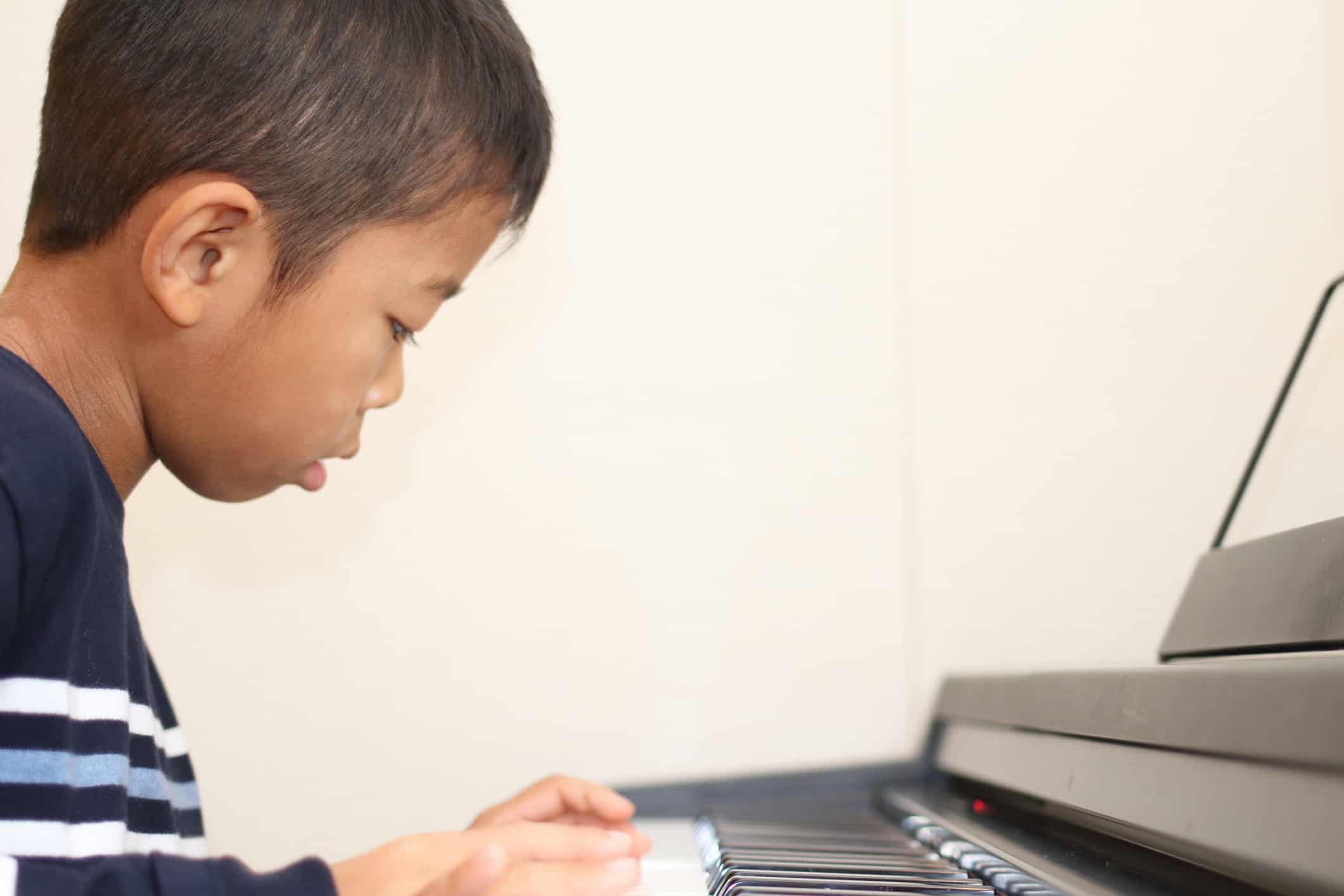 Young male student engaged in learning to play piano on digital piano
