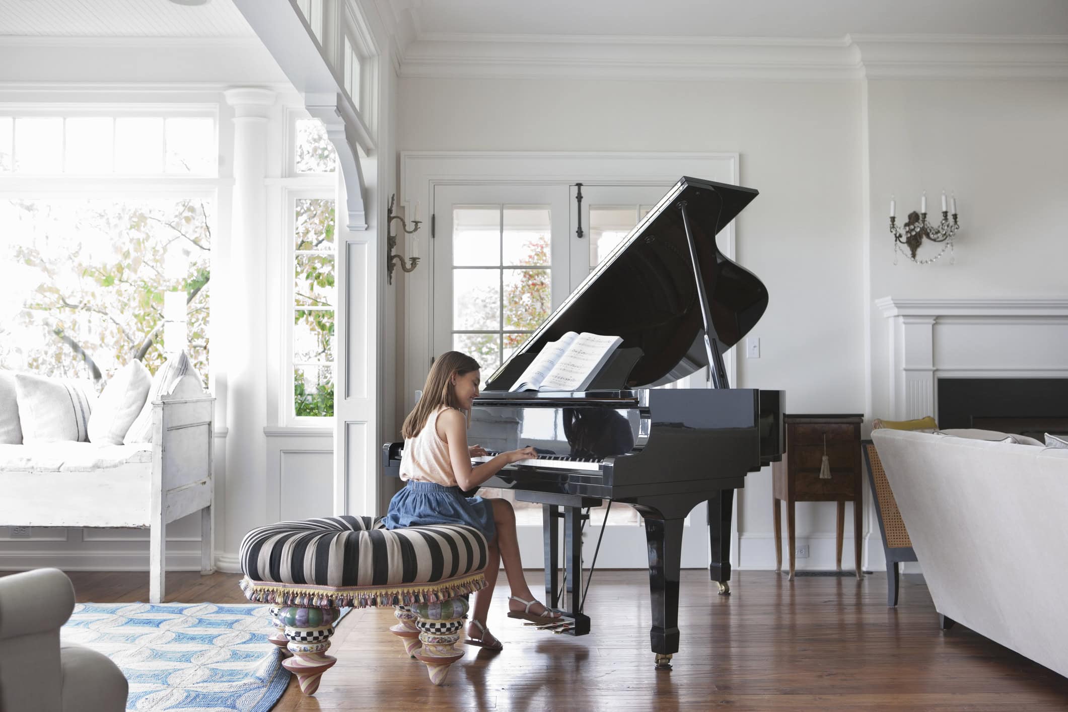 Smiling girl playing baby grand piano in living room of home.